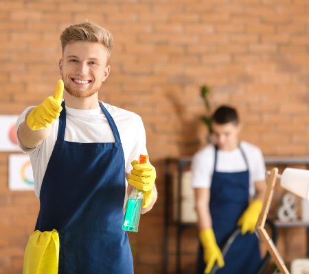 Male janitor showing thumb-up gesture in office during cleaning
