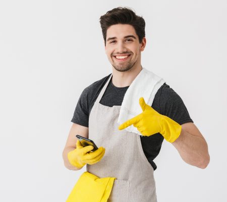 Handsome brunette houseman wearing apron standing isolated over white background, showing mobile phone